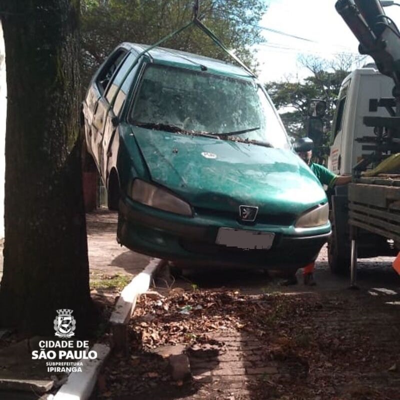 Um carro abandonado na cor verde sendo recolhido por um guincho